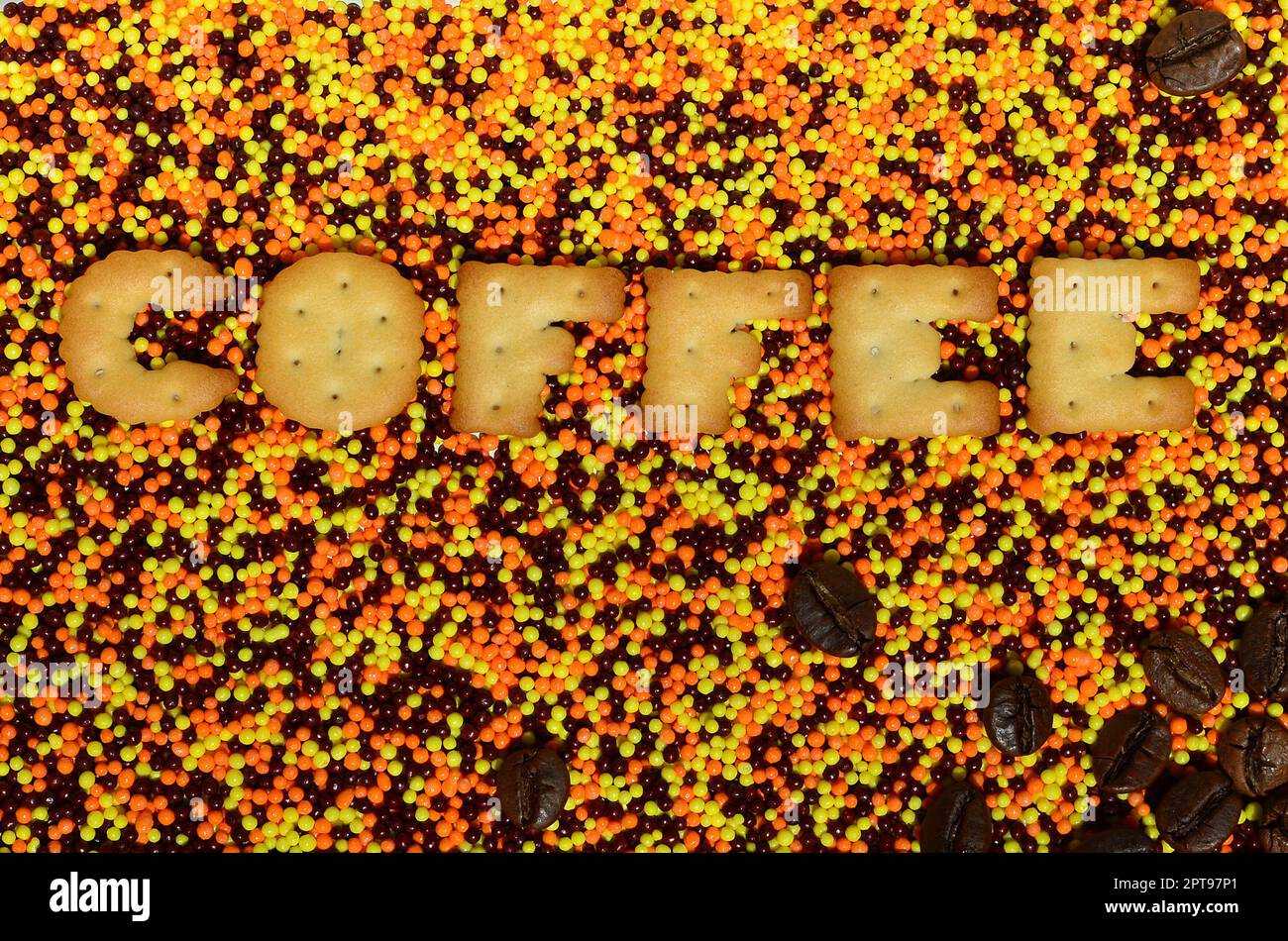 Kaffee. Das Wort der essbaren Cracker-Buchstaben liegt auf dem glasierten Pulver. Eine große Anzahl süßer, farbenfroher Perlen von sehr kleiner Größe zur Dekoration o Stockfoto