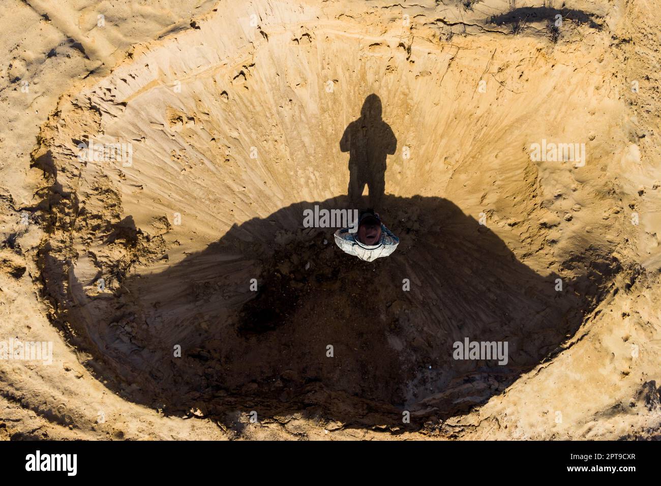 Draufsicht eines Mannes, der in einem Sandloch steht, das wie ein Mondkrater aussieht Stockfoto