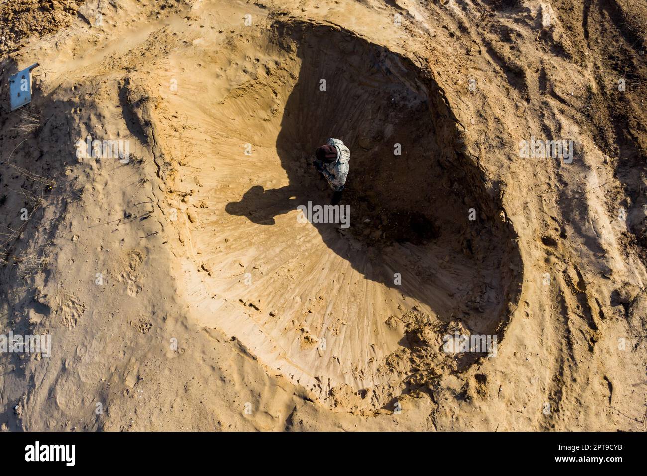 Draufsicht eines Mannes, der in einem Sandloch steht, das wie ein Mondkrater aussieht Stockfoto