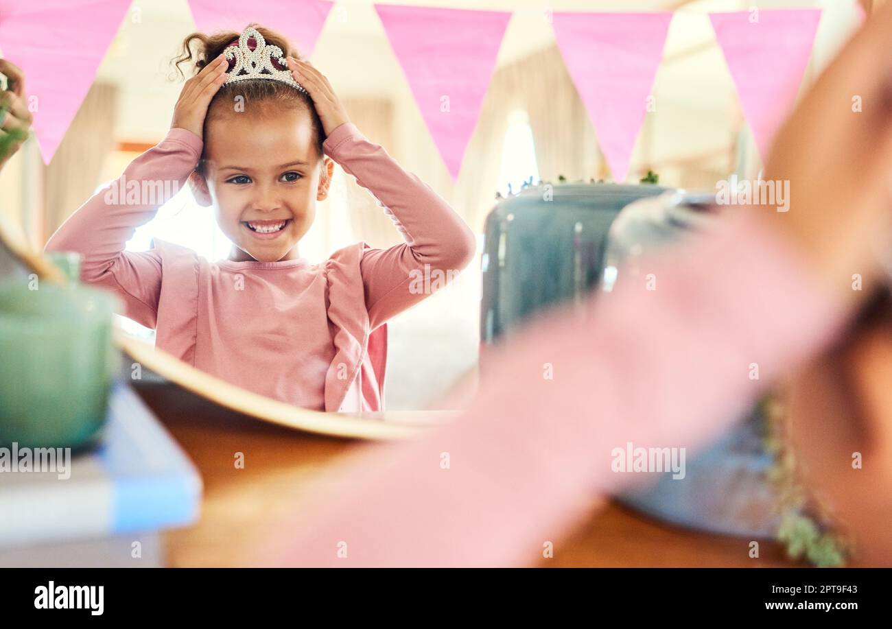 Lass deine Krone nie fallen. Ein kleines Mädchen, das zu Hause eine Krone im Spiegel aufsetzt Stockfoto