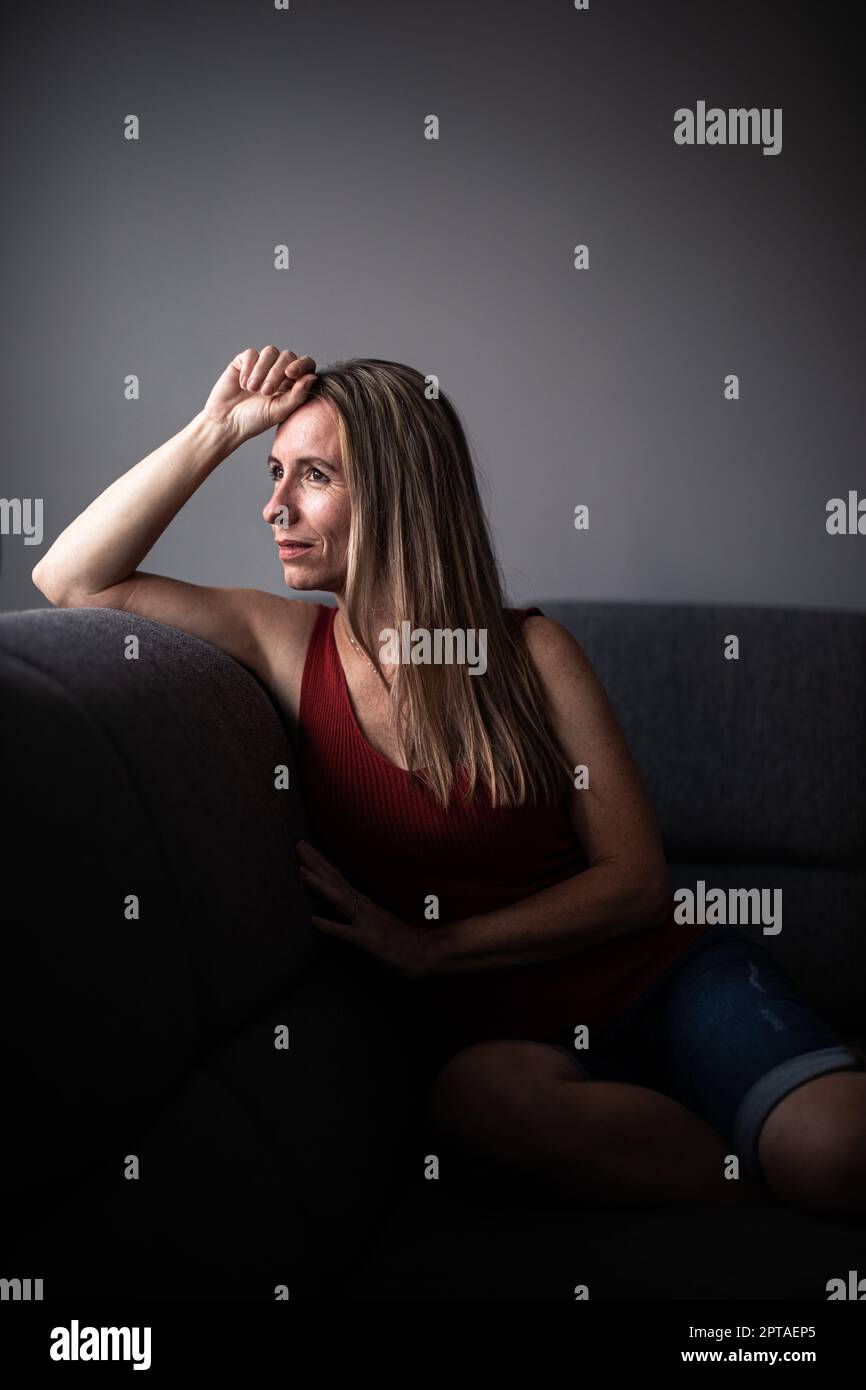 Frau mittleren Alters zu Hause, die sich auf einem Sofa entspannt (farblich abgetöntes Bild) Stockfoto