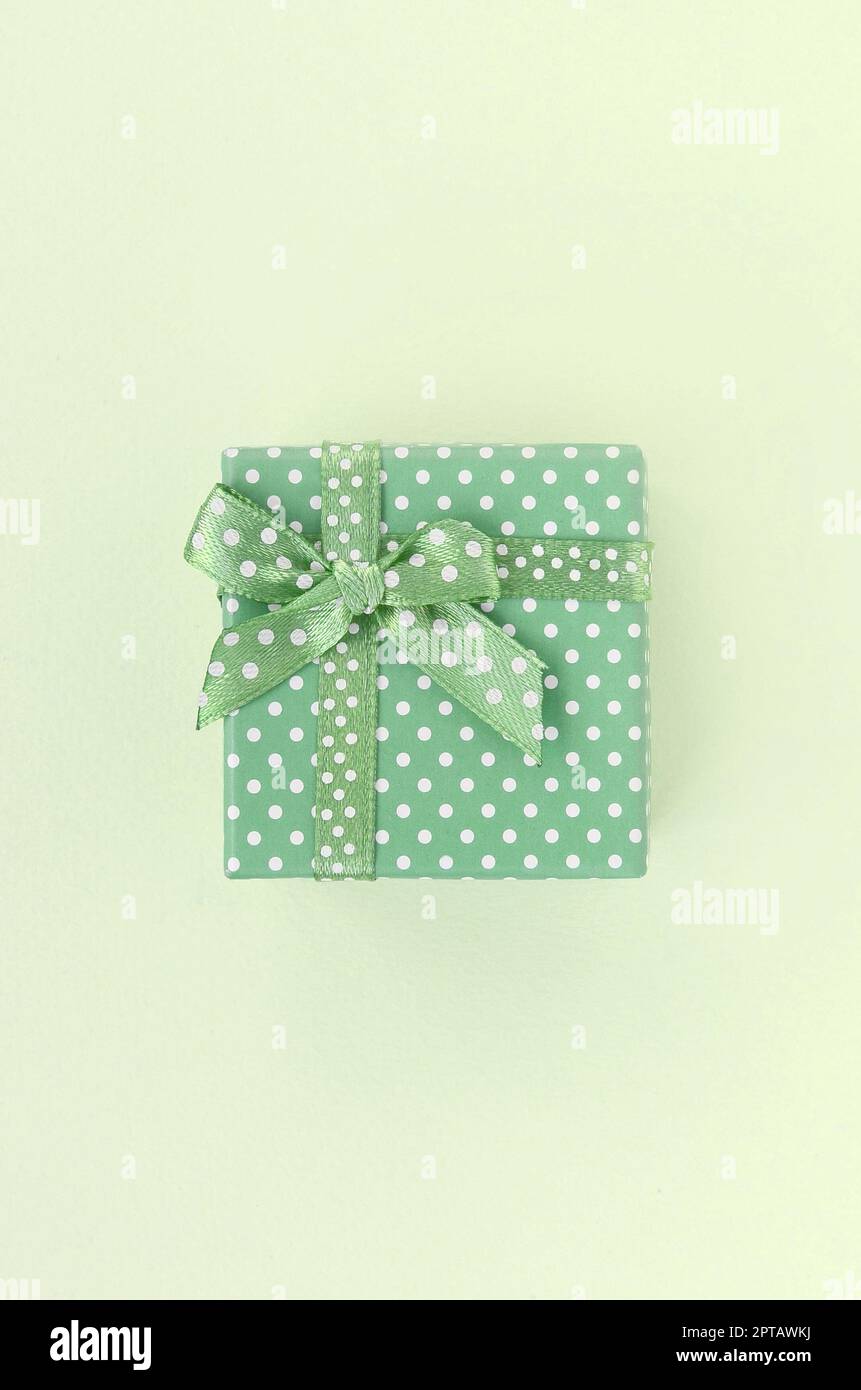 Kleine grüne Geschenkbox mit Schleife liegt auf einem Kalk Hintergrund. Minimalismus flach Ansicht von oben. Stockfoto