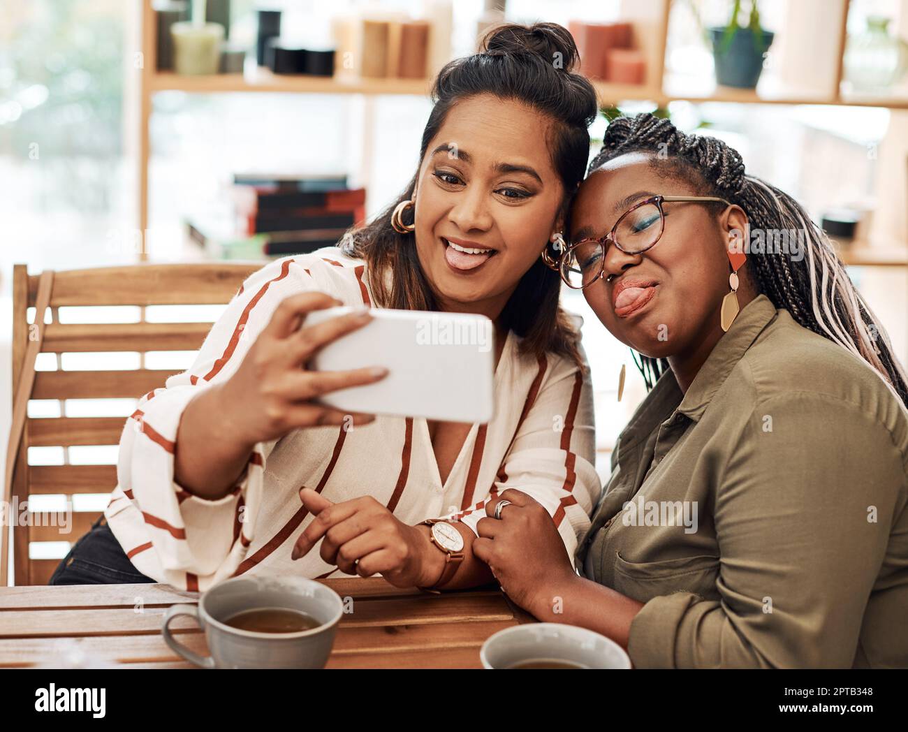 Ich fand meine Seelenverwandte in Dummheit. Zwei junge Frauen machen Selfies im Café Stockfoto