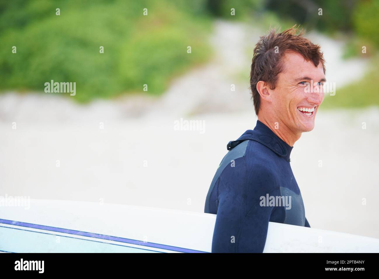 Raus auf die Wellen. Ein junger Surfer, der sein Brett am Strand trägt Stockfoto