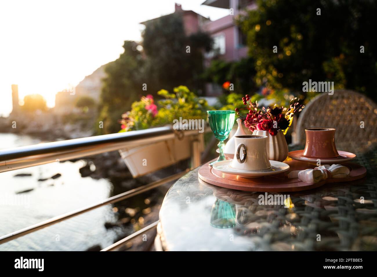 Vorderansicht Nahaufnahme der traditionellen türkischen Kaffeetassen, die draußen mit Wasserblumen serviert werden, und das Dessert in romantischer Umgebung auf einem Glastisch bei Sonnenuntergang Stockfoto