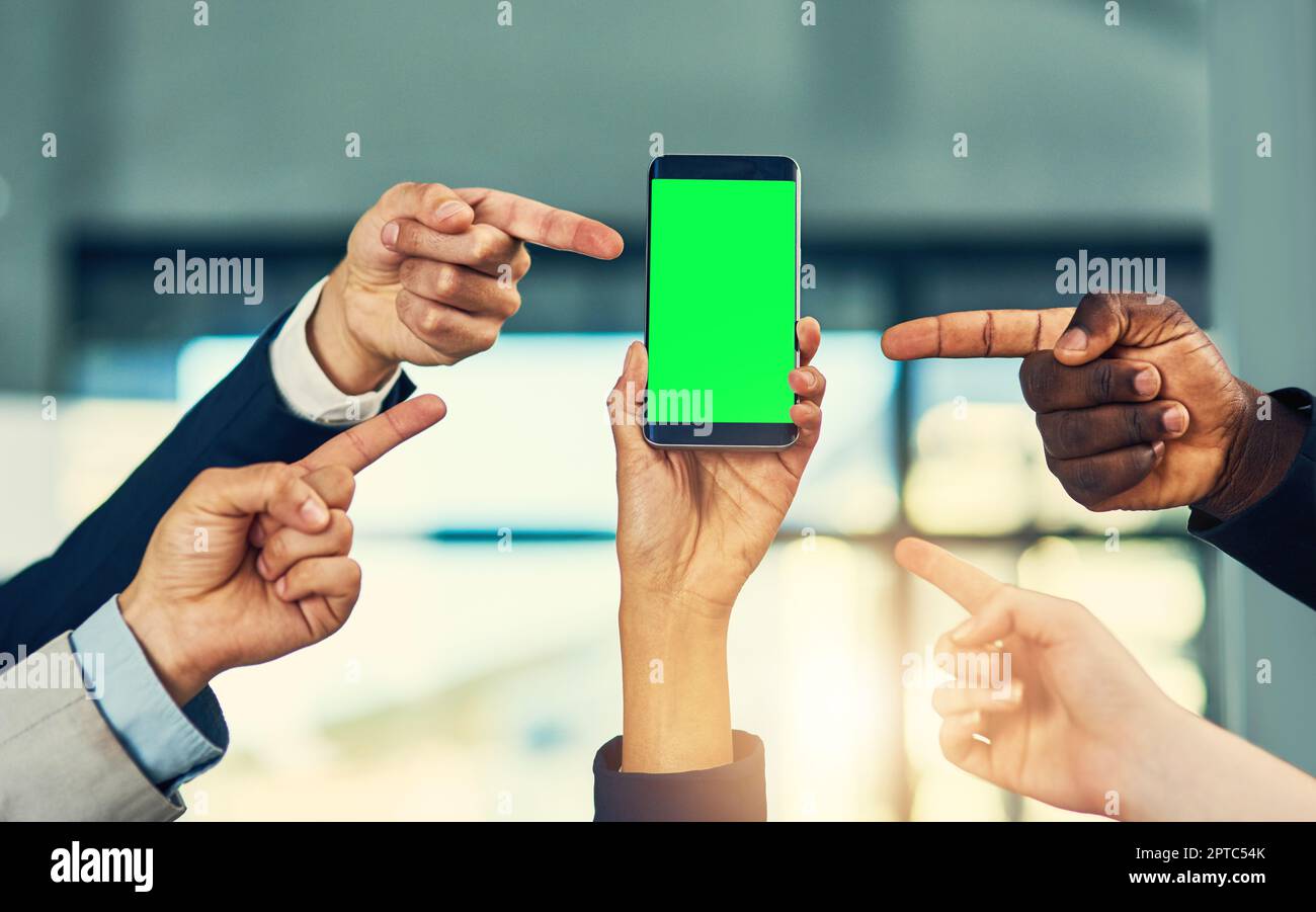 Diese App ist einfach genial. Eine Gruppe von Geschäftsleuten, die auf den grünen Bildschirm eines Mobiltelefons in einem modernen Büro zeigen Stockfoto