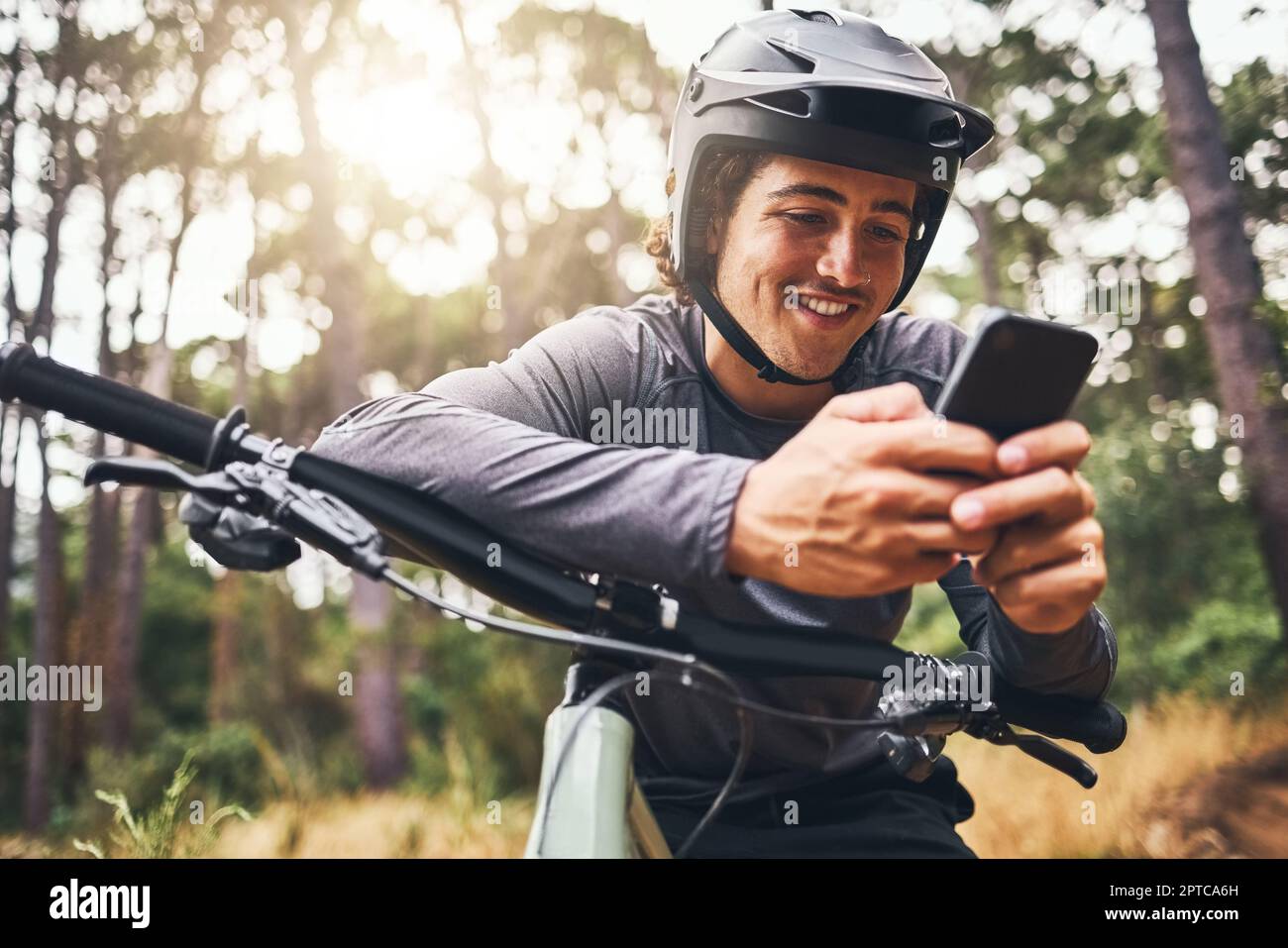 Fitness, Fahrrad und Telefon mit Mann, der SMS schreibt und in einem Wald radelt, glücklich und in der Natur mit Radfahrer entspannen. GPS, Internet und Karte mit Sportsendungen für Männer Stockfoto