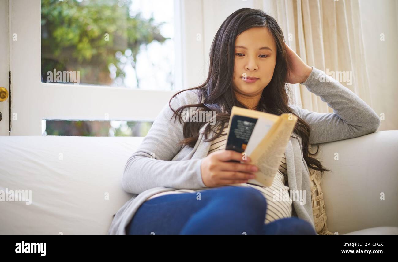 Ich lese über das kleine Ding der Schwangerschaft. Eine schwangere Frau, die zu Hause ein Buch liest Stockfoto