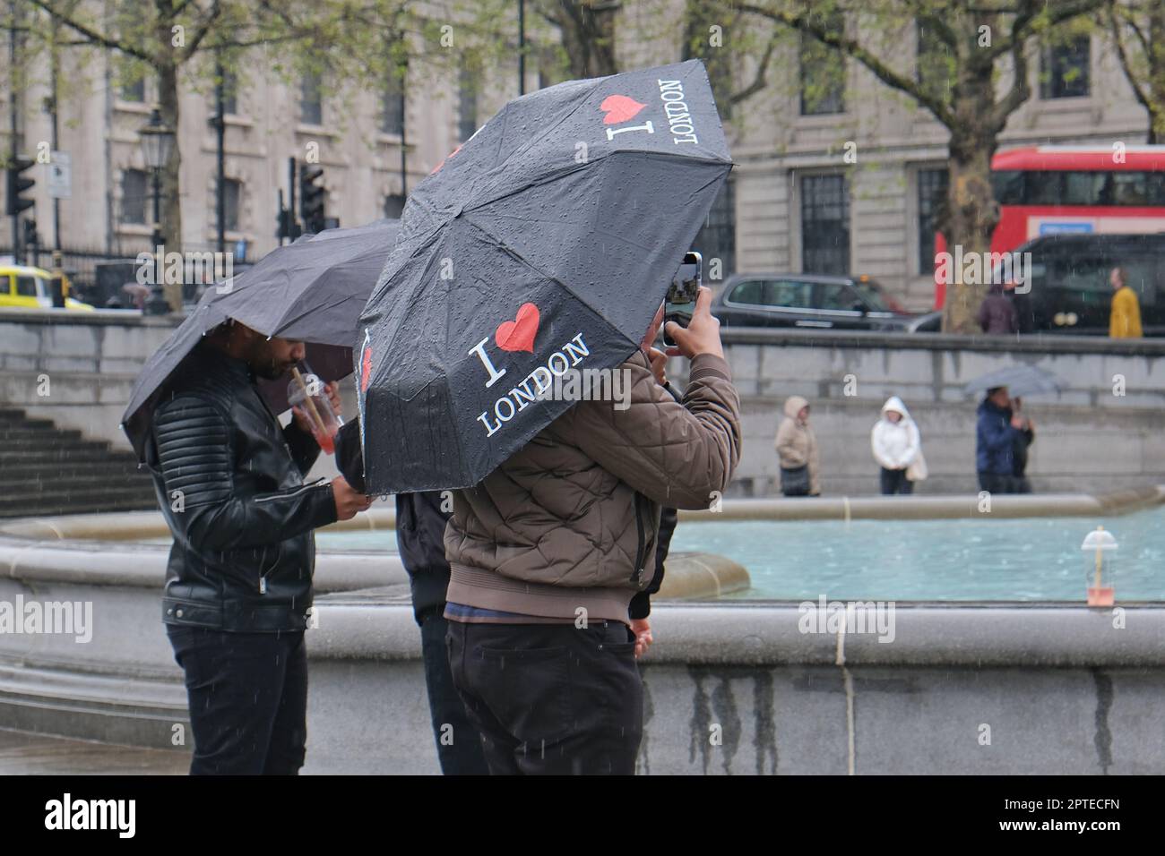 London, Großbritannien. Zwei Touristen fotografieren am Trafalgar Square, während sie sich unter den Sonnenschirmen von I Heart London verstecken. Stockfoto