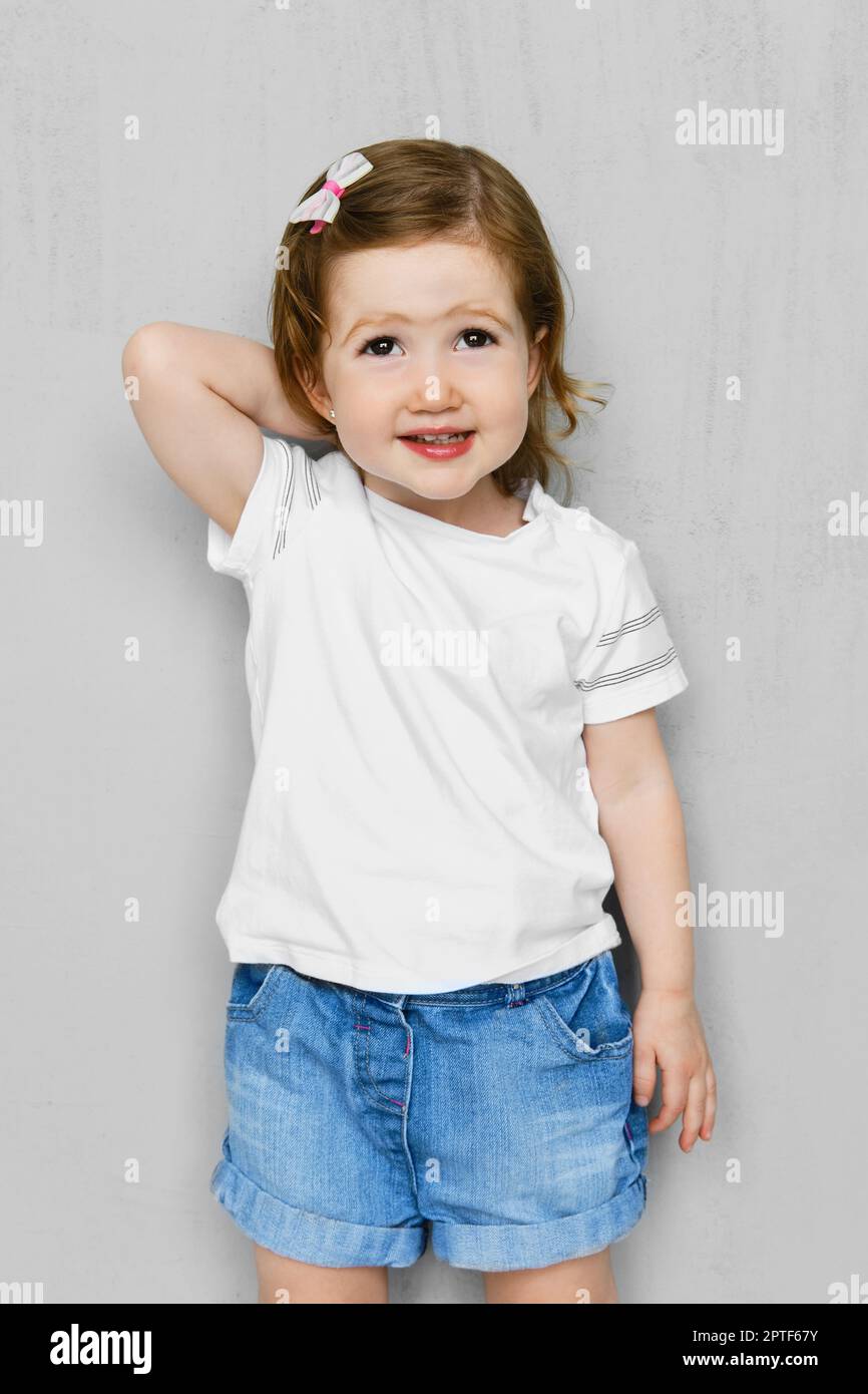 Zwei Jahre altes Mädchen in weißen T-Shorts und Jeans Shorts posiert im Studio Stockfoto
