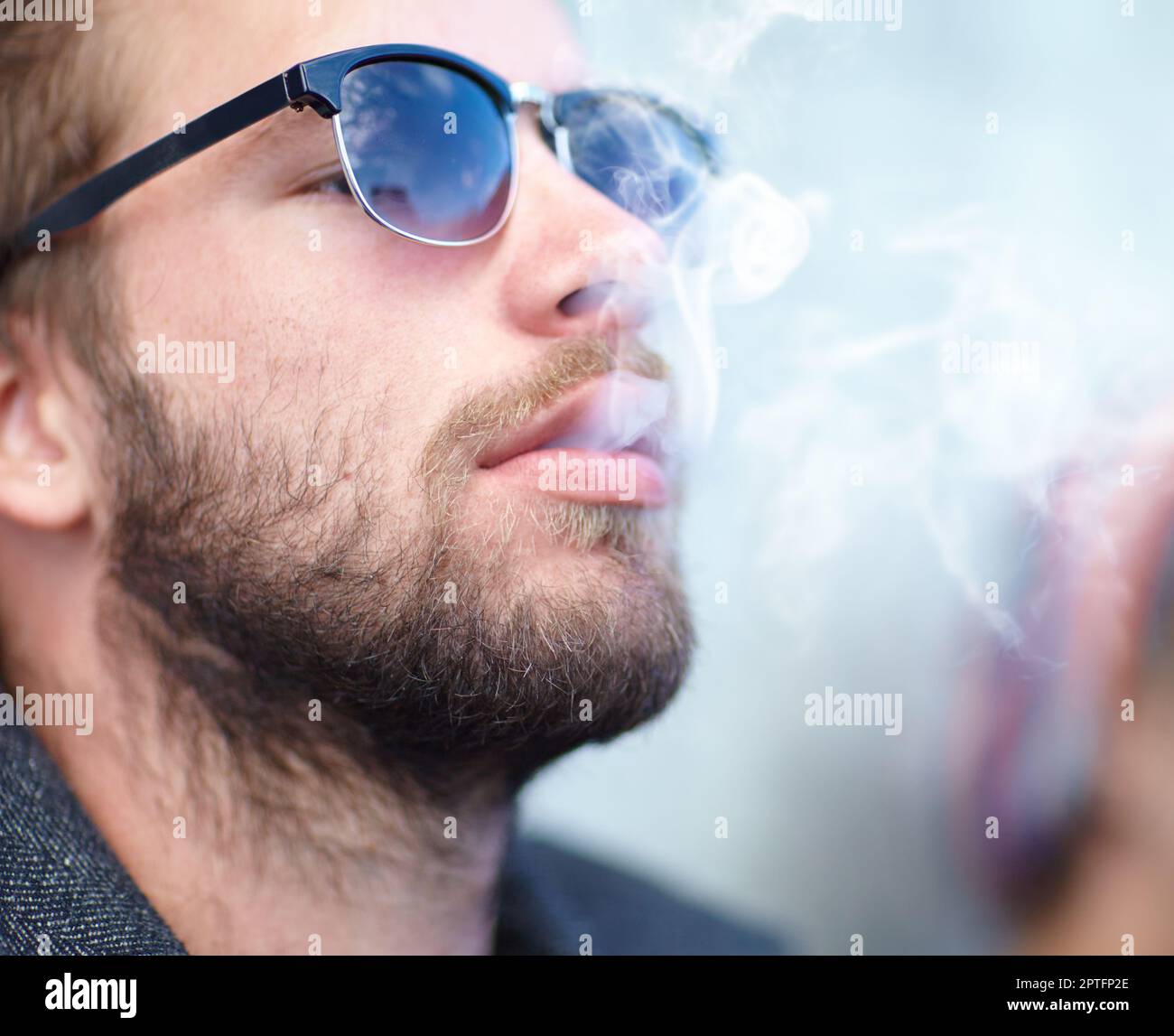 Alte Gewohnheiten sterben hart. Ein gutaussehender Mann, der Hipster mit Sonnenbrille raucht und raucht Stockfoto