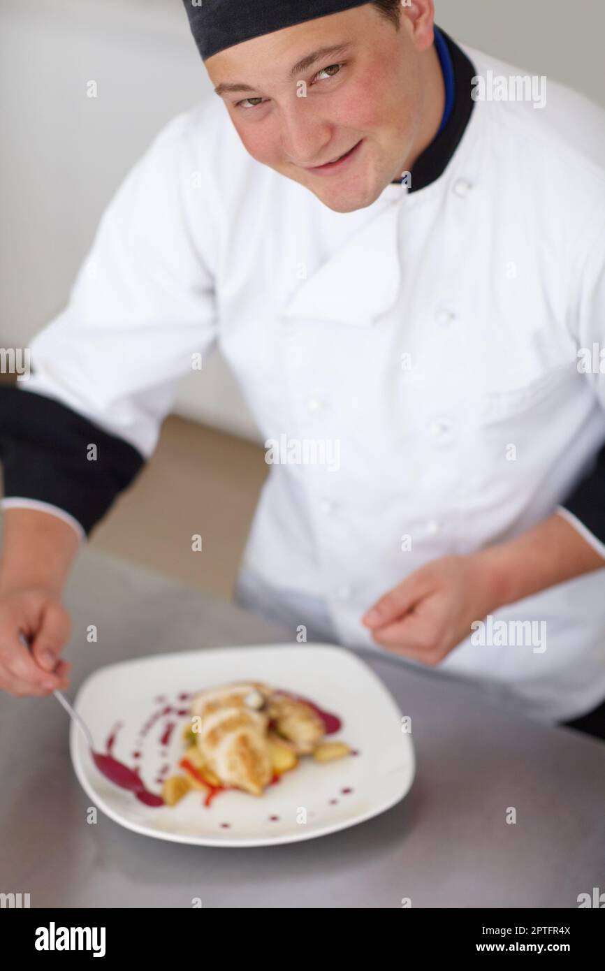 Mit dem letzten Schliff wird es perfekt. Yougn Chefkoch, der einem vorbereiteten Hähnchengericht dekorative Garnierung hinzufügt - Porträt Stockfoto