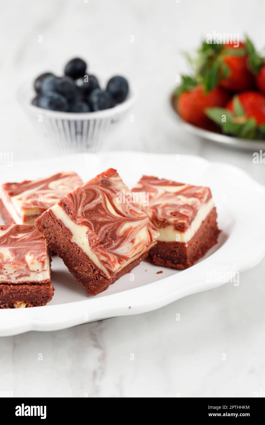 Rote Samt-Brownies mit Käse auf weißem Keramikteller. Gebackener roter Teig mit Sahnekäse-Marmorbrownie Stockfoto