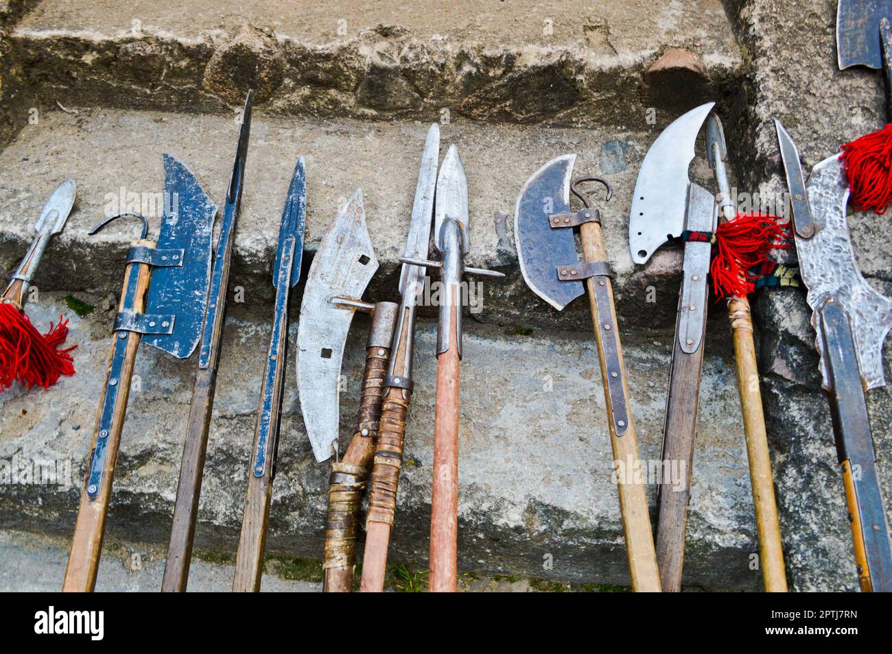 Die alten mittelalterlichen kalten Waffen, Äxte, Olibarden, Messer, Schwerter mit Holzgriffen lecken auf den Steintreppen des Schlosses. Stockfoto