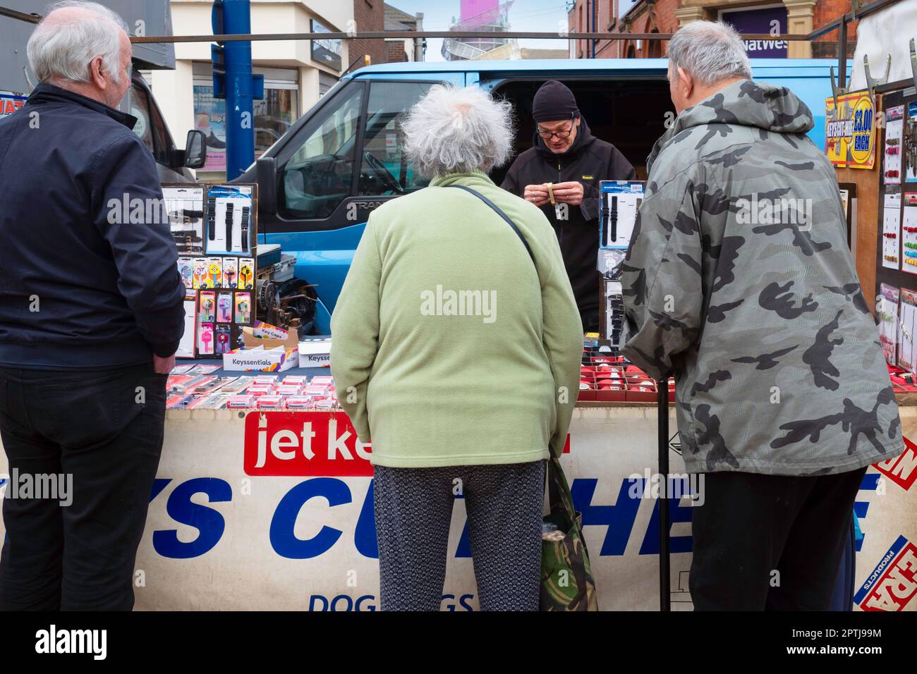 Der Halter repariert ein Uhrarmband an einem Stand auf dem Wochenmarkt, wobei drei Kunden Redcar High Street Cleveland England UK anschauen Stockfoto