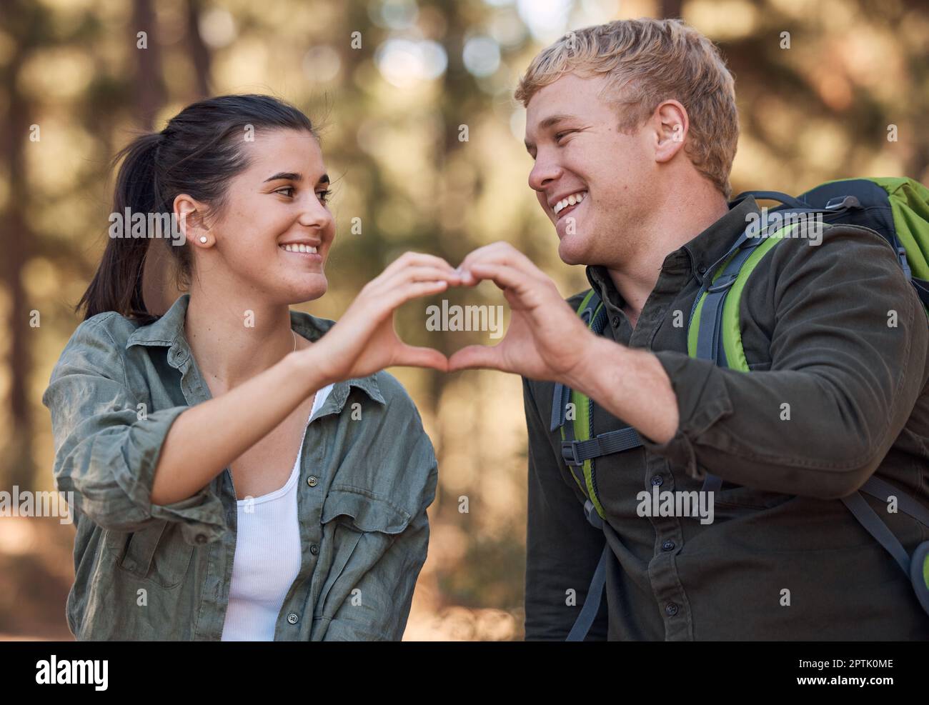 Liebe, Paar und Herzhände während der Wanderung in der Natur für Zuneigung oder Unterstützung. Emoji, Handgeste und Romantik oder Intimitätsform mit glücklichem Mann und Wom Stockfoto