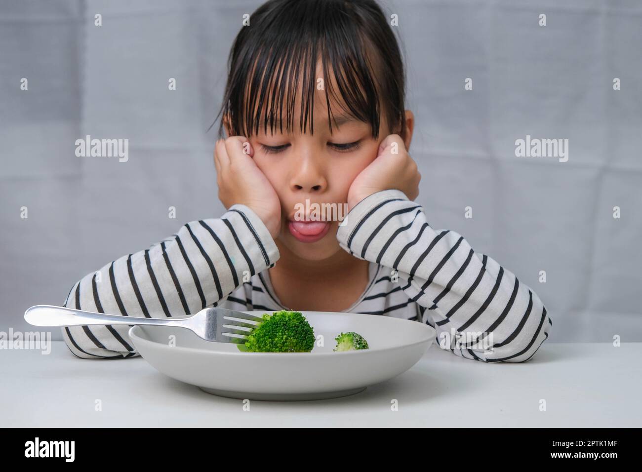 Kinder essen kein Gemüse. Süßes asiatisches Mädchen weigert sich, gesundes Gemüse zu essen. Ernährung und gesunde Ernährungsgewohnheiten für Kinder. Stockfoto