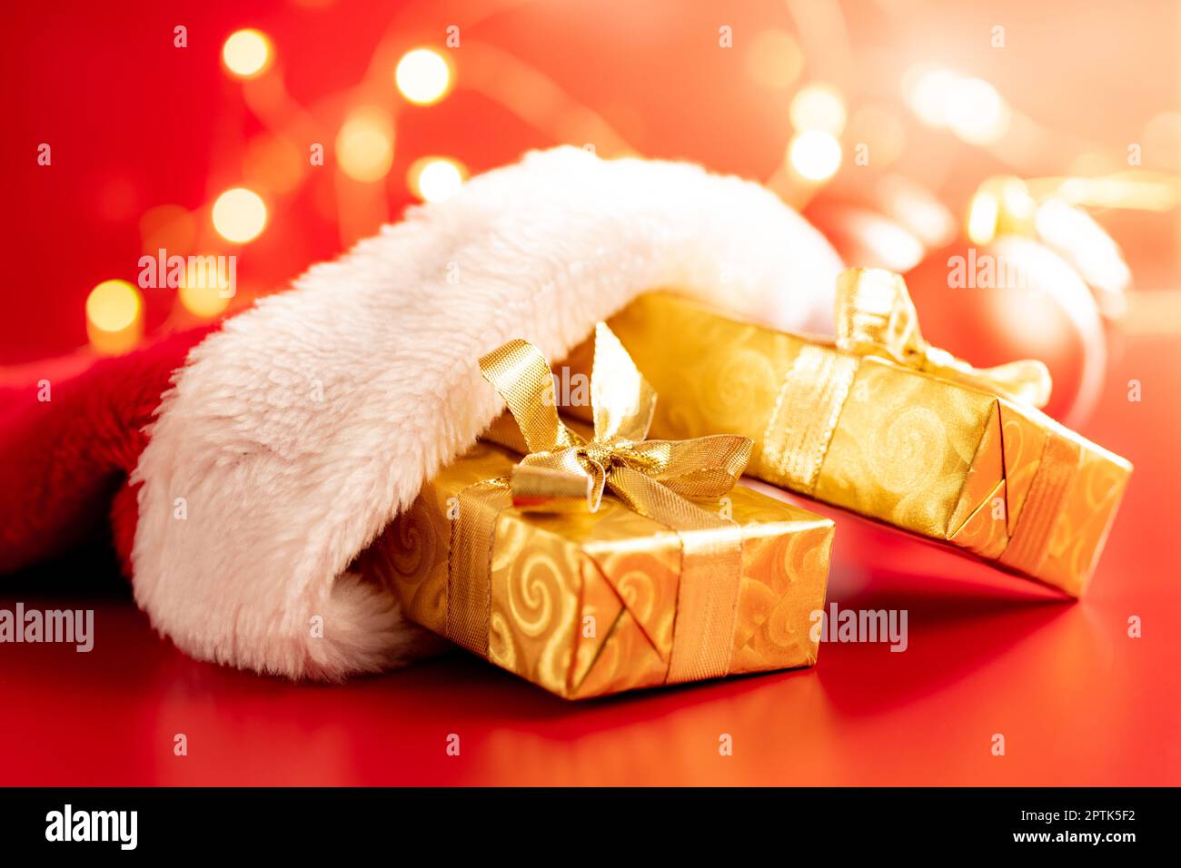 Goldenes weihnachtsgeschenk in rotem Weihnachtsmütze auf rotem Hintergrund. Stockfoto