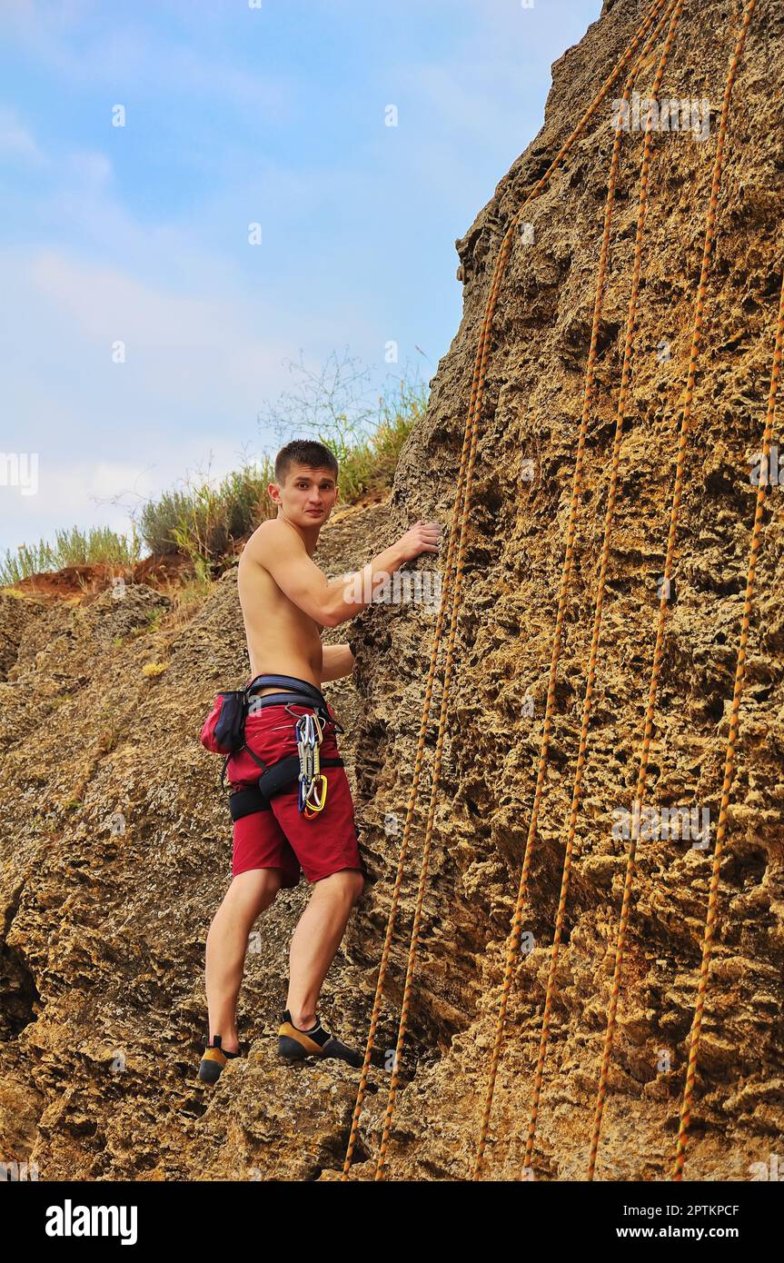 Junger Kletterer, der an einem Seil auf einen Felsen klettert Stockfoto