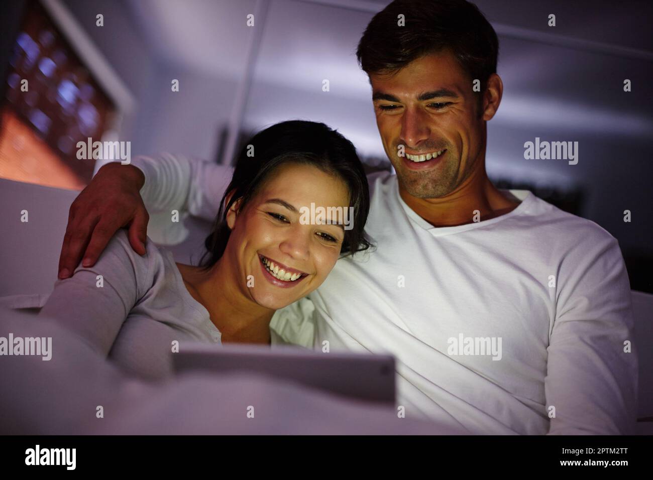 Rom-Coms sind ihre Lieblingsfilme. Ein Paar sieht sich Filme auf einem digitalen Tablet an, während es im Bett sitzt Stockfoto