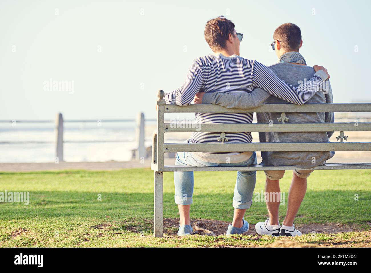 Ich liebe das Meer. Rückblick auf ein junges schwules Paar, das auf einer Parkbank sitzt Stockfoto