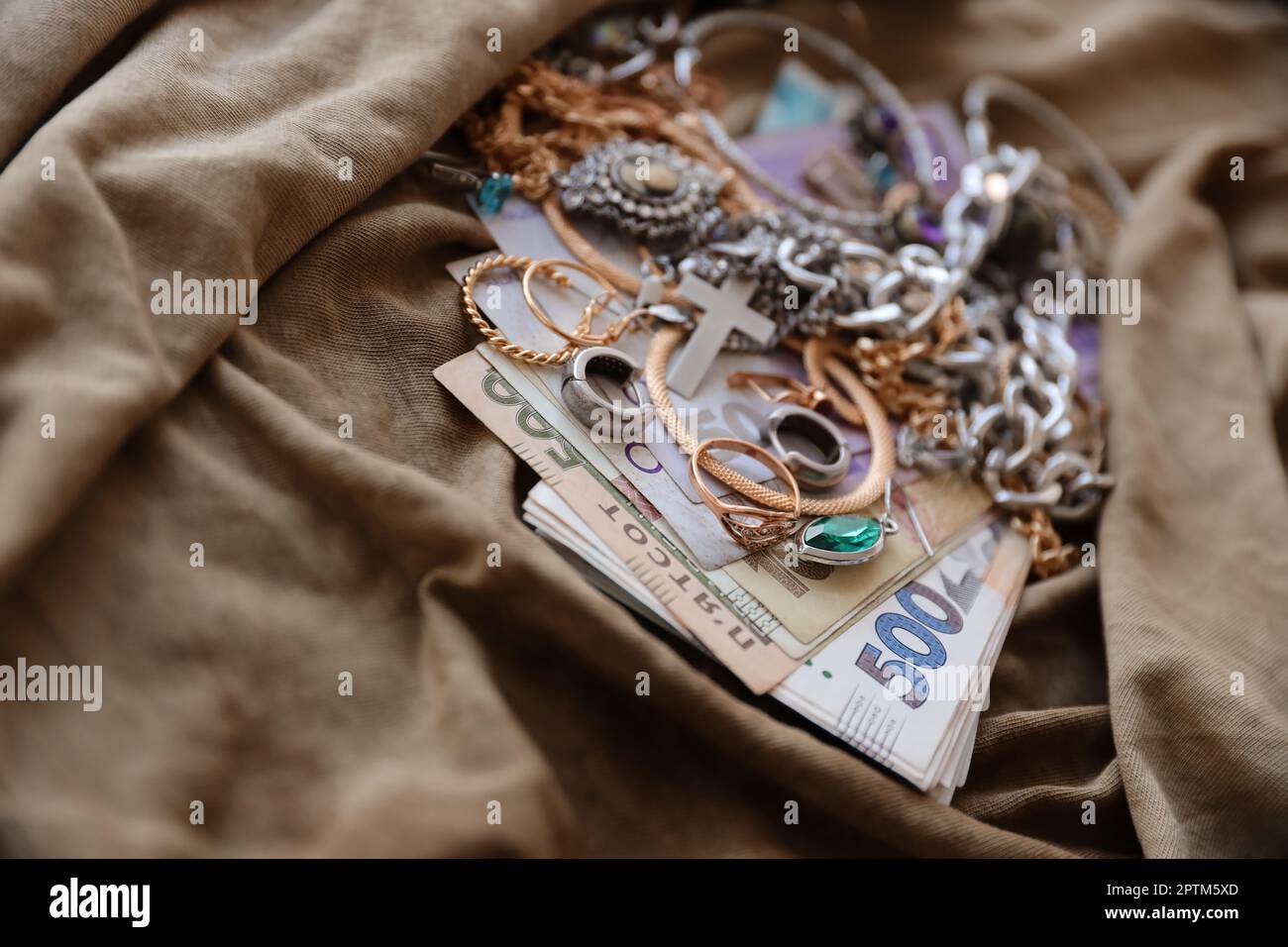 Haufen gestohlener Schmuck und Geld auf Militäruniform Stoff. Plünderung durch russische Soldaten in ukrainischen Städten während des russischen Angriffs auf U Stockfoto