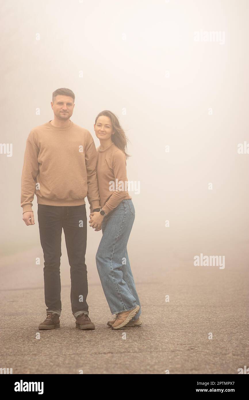 Eine junge, traditionelle verheiratete Familie, ein Mann und eine weiße Frau, die Händchen halten, laufen an einem Frühlingsmorgen in dickem Nebel, sie sind gut gelaunt Stockfoto