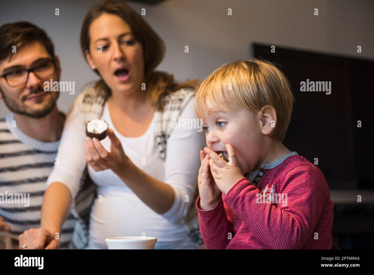 Kleiner Junge, der mit offenem Mund Nachtisch isst, während die Eltern schockiert sind, München, Deutschland Stockfoto