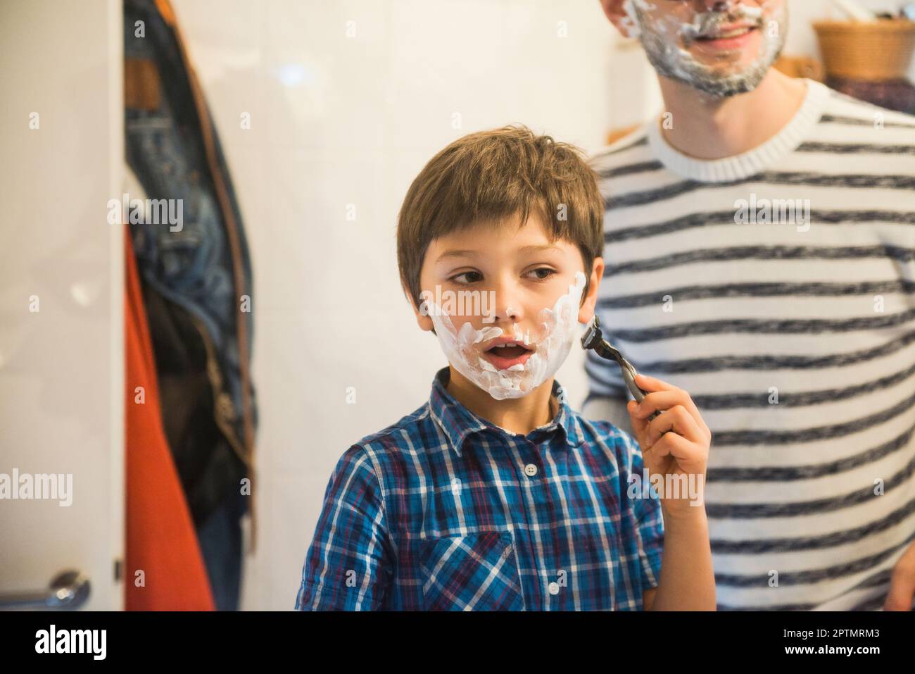 Sohn rasiert sich im Bad, während Vater Uhren, München, Deutschland Stockfoto