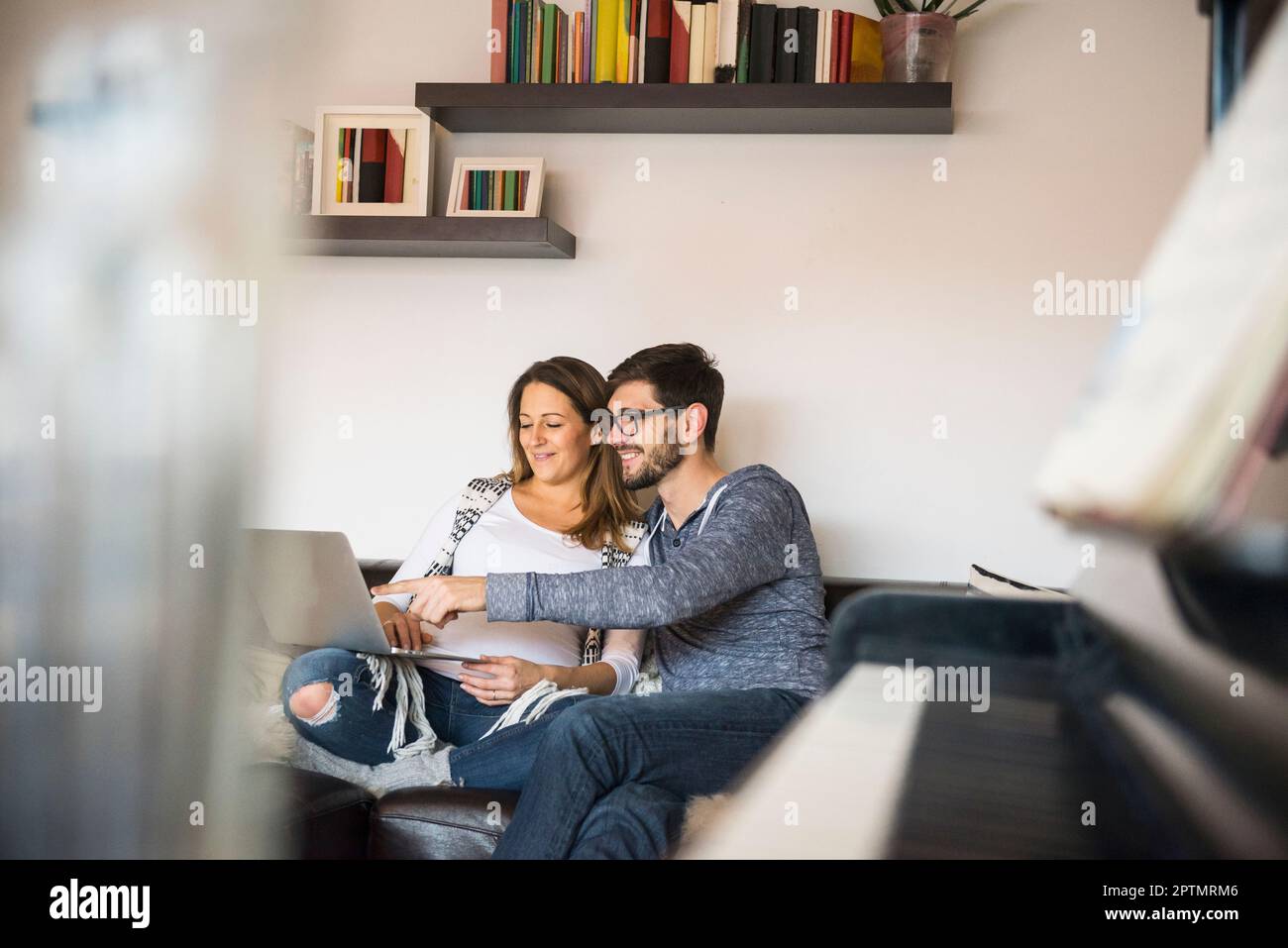 Schwangere Frau und Ehemann mit Laptop auf Sofa, München, Deutschland Stockfoto