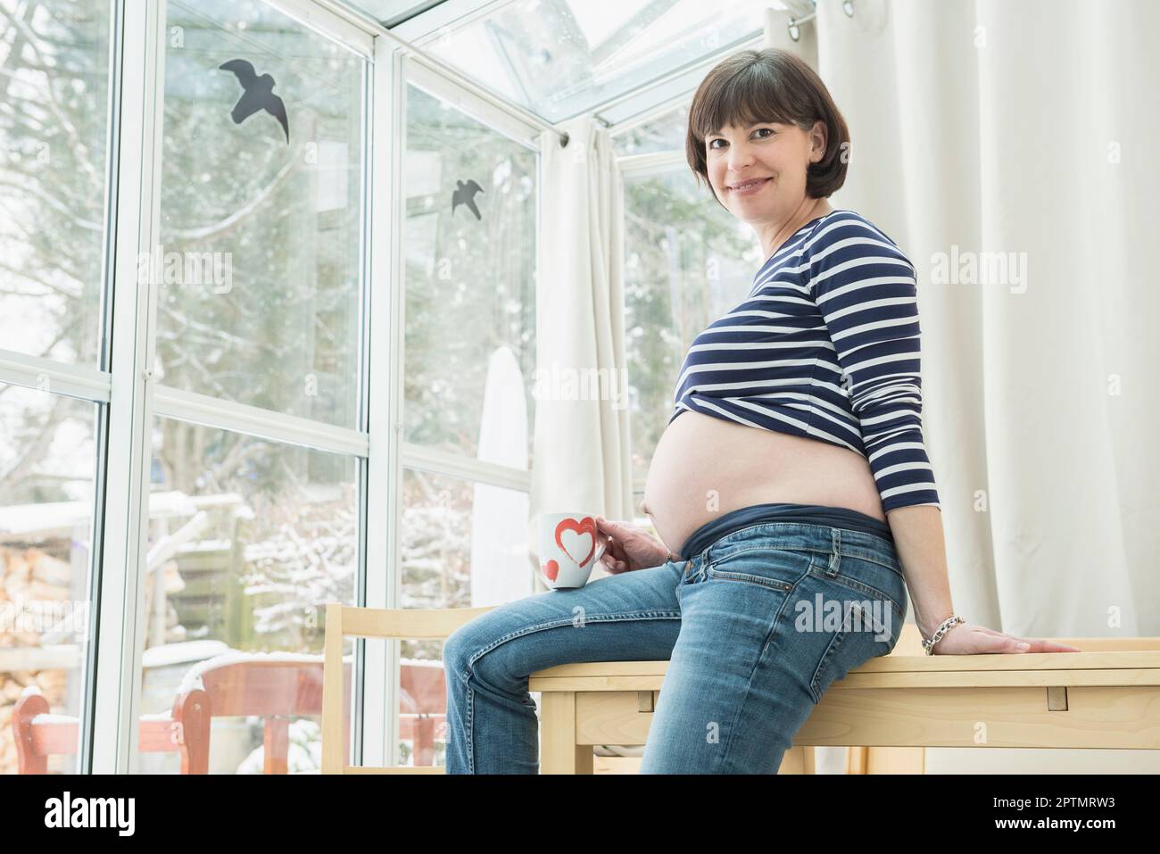 Porträt einer schwangeren Frau, die mit einer Kaffeetasse auf dem Tisch sitzt Stockfoto