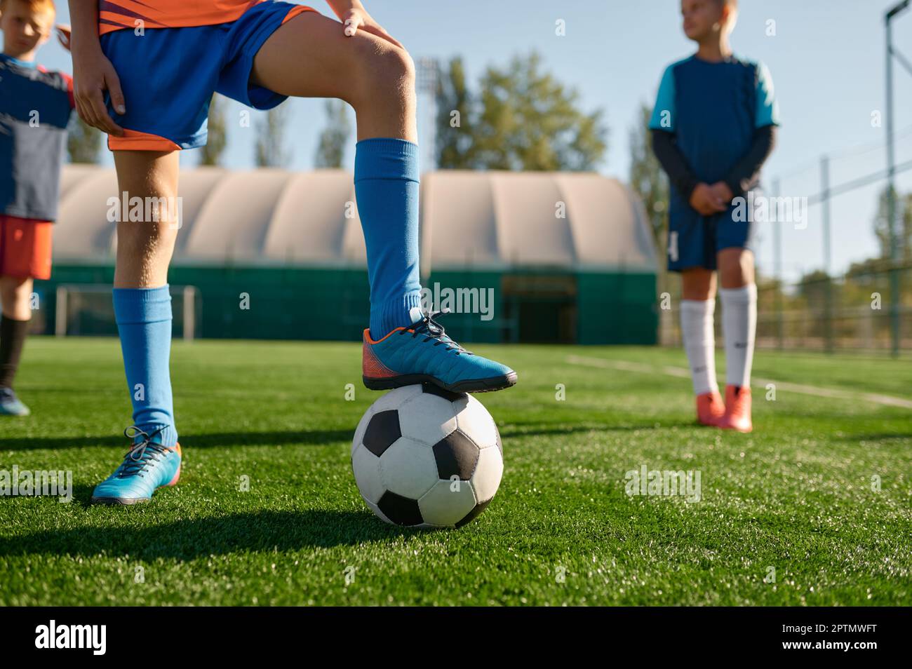 Ein junger Fußballspieler, der Stiefel auf einem kurzen Schlag hält. Ein Kinderteam, das Fußball auf dem Rasen trainiert Stockfoto