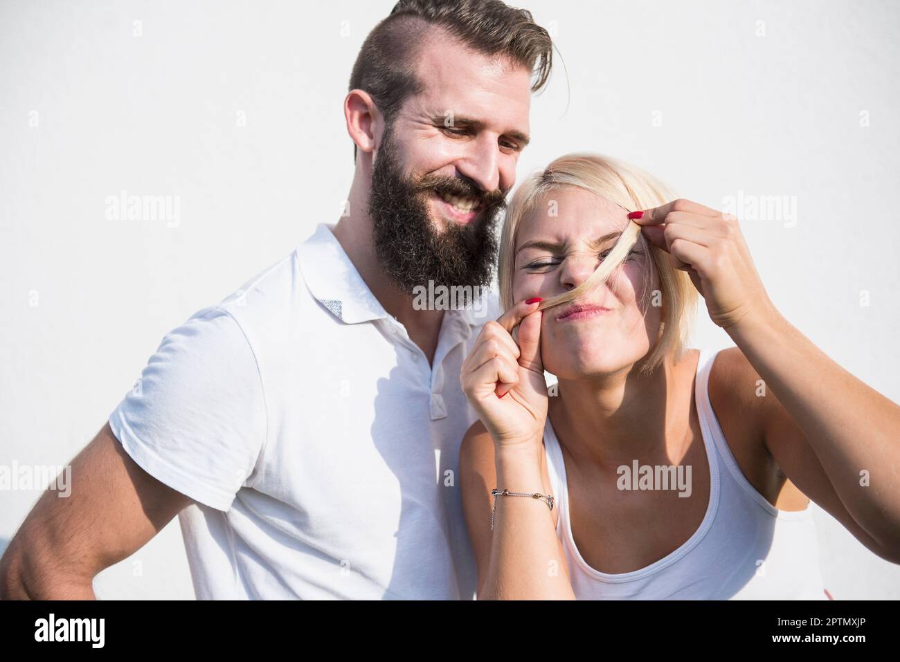 Ein junger Mann, der mit seiner verspielten Freundin lächelt und Schnurrbart mit Haaren macht, Bayern, Deutschland Stockfoto