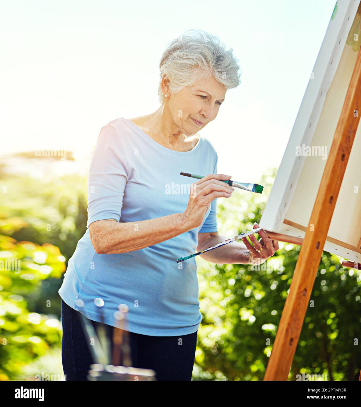 Sie ist präzise, wenn es um Malerei geht. Eine Seniorin, die im Park malt. Stockfoto