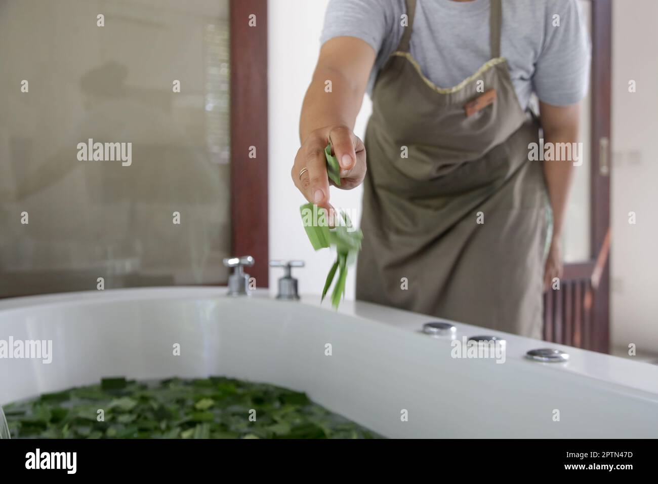 Eine Frau, die ein natürliches Kräuterbad vorbereitet. Spa-Leckereien: Regenerierendes Kräuterbad mit Limettenscheiben, Zitronengrasblättern und Blumen. Stockfoto