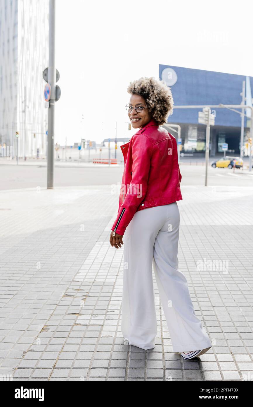 Rückansicht einer Frau in pinkfarbener Jacke, die die Straße entlang läuft Stockfoto