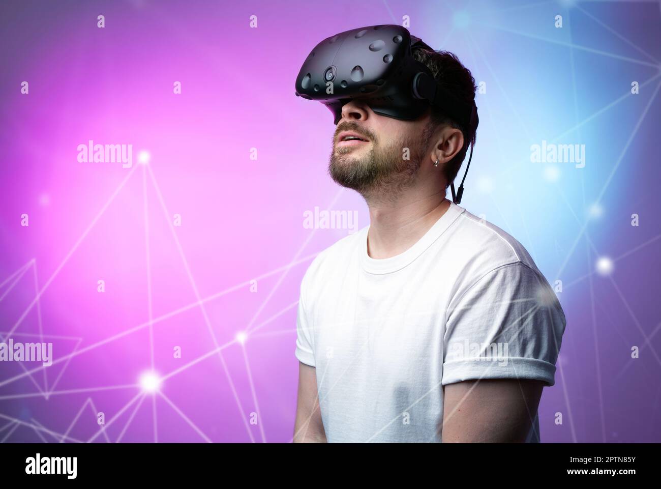 Ein Typ mit VR-Brille von Virtual Reality auf einem farbigen Hintergrund mit Raumgradient. Genießen Sie moderne Technologien, erweiterte Realität, Metaverse und Spiele. Hobby Stockfoto