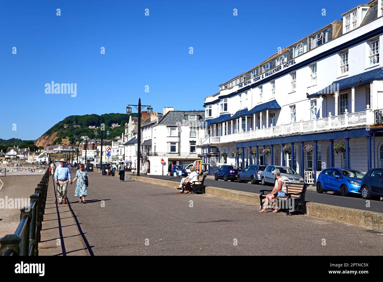 Touristen genießen die Aussicht entlang der Promenade mit dem Strand auf der linken Seite und dem Royal York and Faulkner Hotel auf der Rückseite, Sidmouth, Großbritannien. Stockfoto