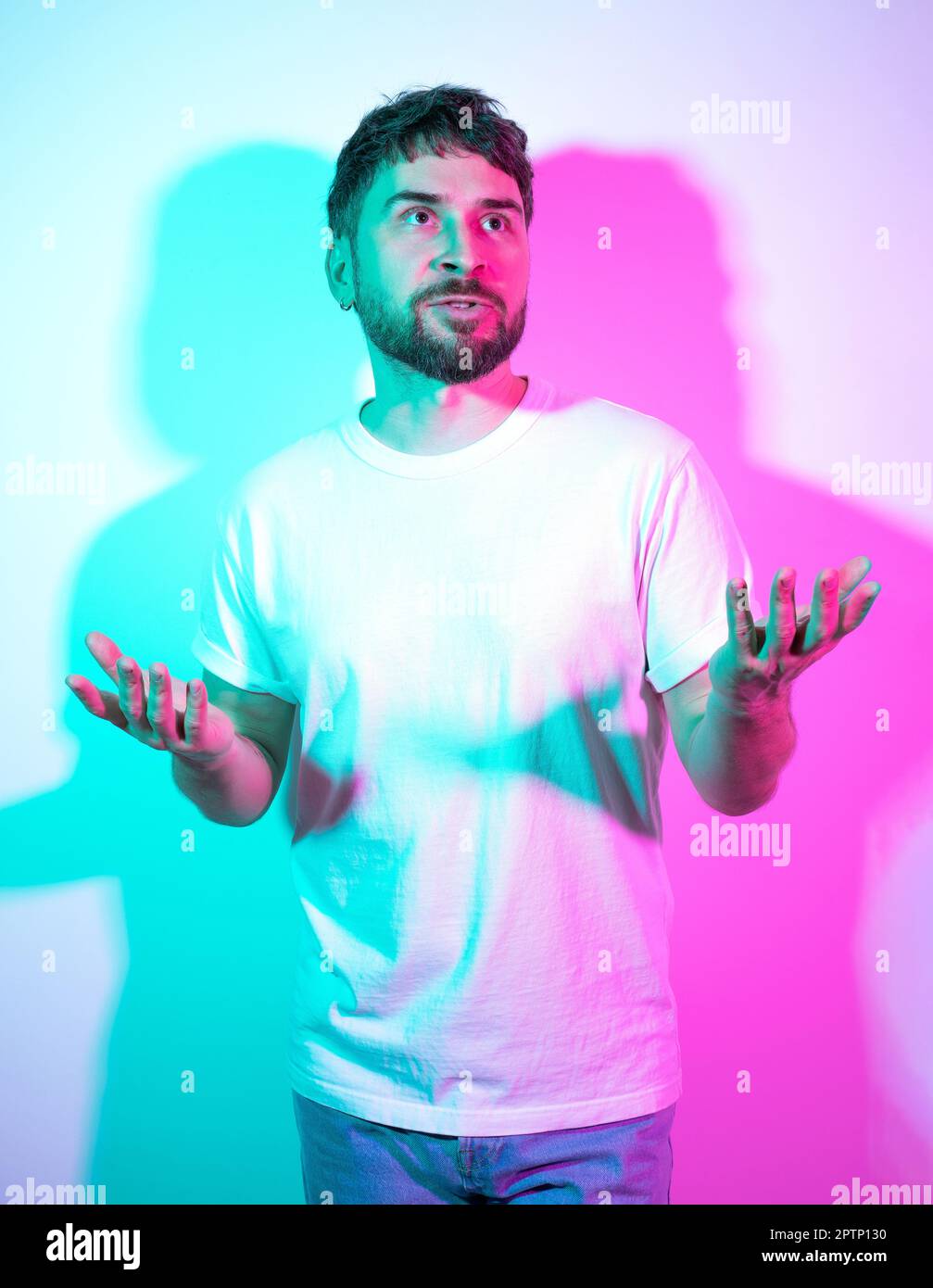Kreatives Porträt mit Bart im mittleren Alter attraktiver Mann im weißen T-Shirt mit leuchtendem Neonhintergrund. Zweifarbige Schatten. Der Mann denkt über eine Wahl nach Stockfoto