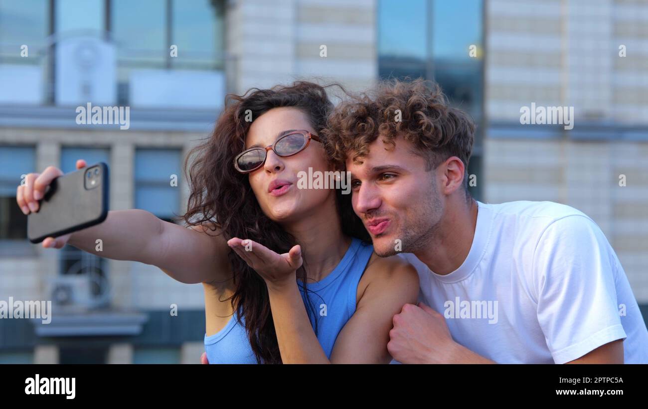 Die Kamera kehrt von einem glücklichen jungen Paar, Freund und Freundin, zurück und macht Selfie-Fotos mit dem Smartphone draußen auf der Party auf dem Dach. Leute feiern Stockfoto