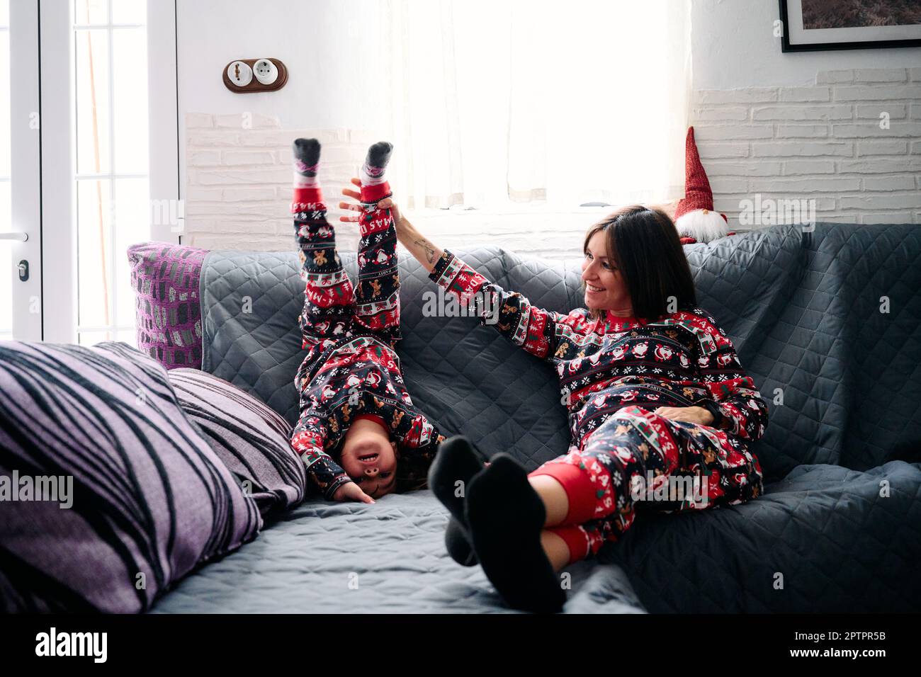 Eine Mutter und eine Tochter im passenden Pyjama, die zu Hause auf dem Sofa spielten. Es fängt die Wärme, Liebe und Zärtlichkeit der besonderen Bindung zwischen einem Mott ein Stockfoto