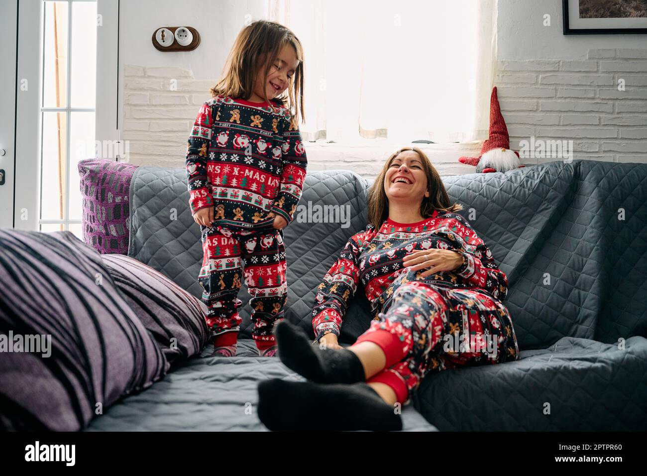 Eine Mutter und eine Tochter im passenden Pyjama, die zu Hause auf dem Sofa spielten. Es fängt die Wärme, Liebe und Zärtlichkeit der besonderen Bindung zwischen einem Mott ein Stockfoto