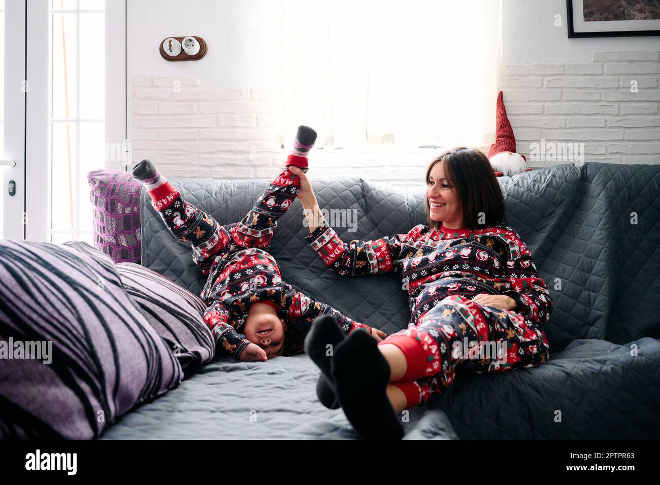 Eine Mutter und eine Tochter im passenden Pyjama, die zu Hause auf dem Sofa spielten. Es fängt die Wärme, Liebe und Zärtlichkeit der besonderen Bindung zwischen einem Mott ein Stockfoto