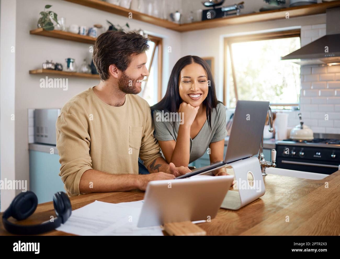 Glücklicher junger Kaukasier, der an einem Laptop arbeitet, während seine Frau neben ihm steht und auf den Bildschirm schaut. Ein Mann, der freiberuflich arbeitet und abgelenkt wird Stockfoto