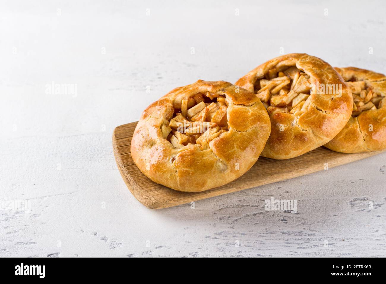 Süße Mini-Pasteten mit Äpfeln und Zimt auf einem Holzbrett mit einer Serviette auf hellgrauem Hintergrund. Köstliches hausgemachtes Essen Stockfoto