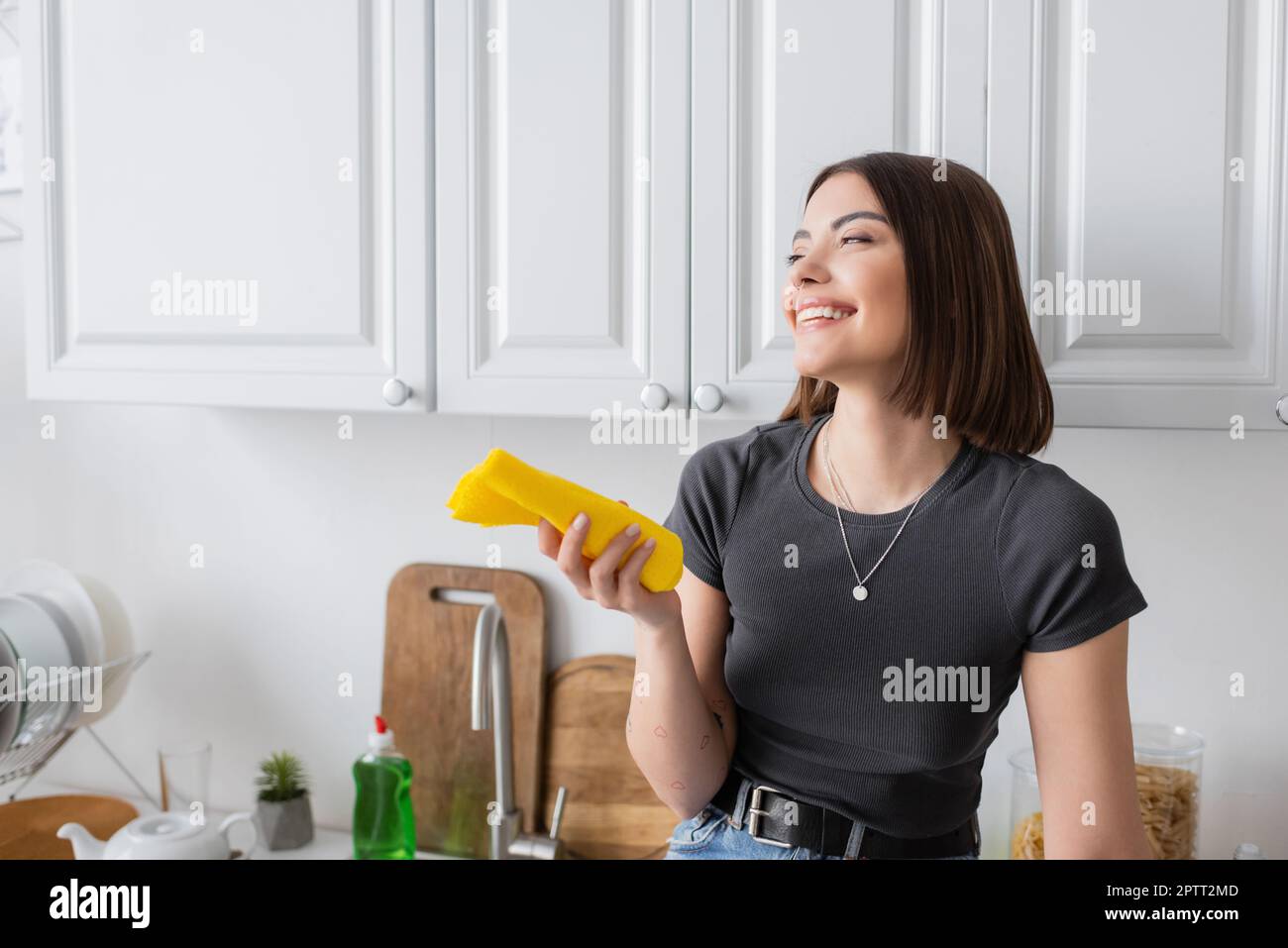 Lächelnde brünette Frau, die einen Lappen hält, während sie zu Hause in der Küche steht, Stockbild Stockfoto