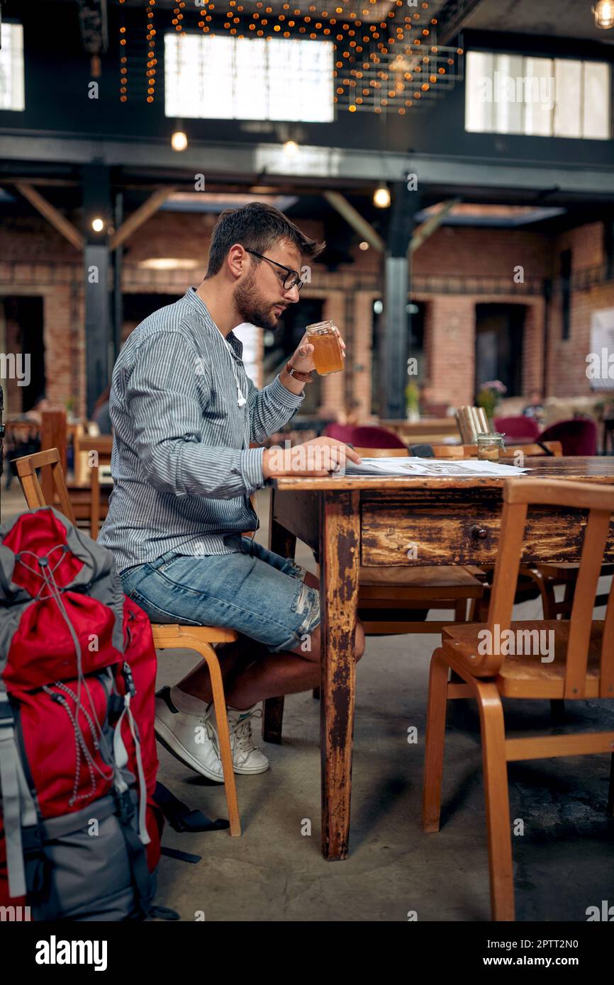 Junger Reisender auf einer Kaffeepause, trinkt und liest Zeitung allein in einem Café. Reisen, Lifestyle, Leibeskonzept. Stockfoto