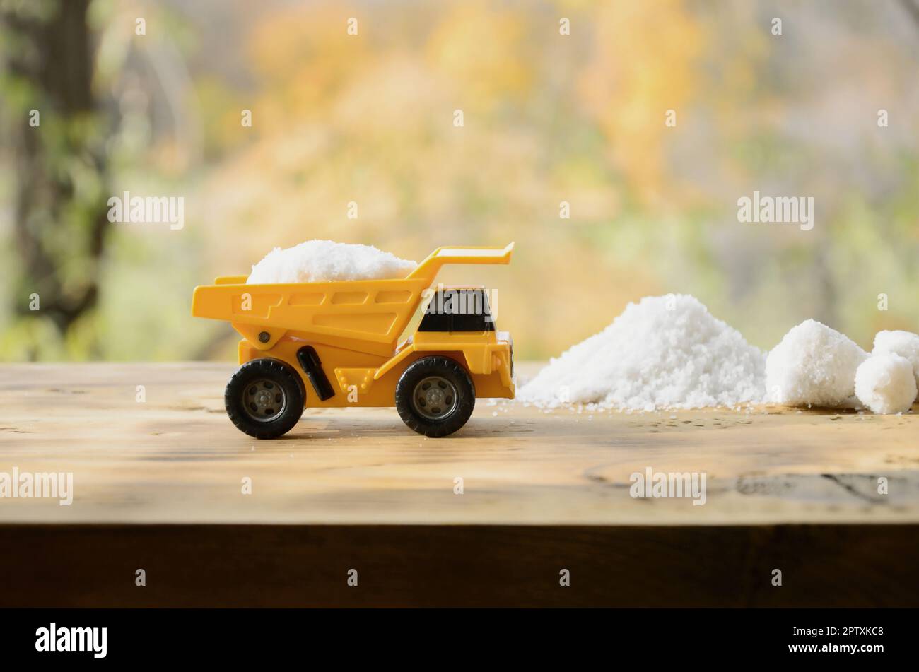 Ein kleines gelbes Spielzeug-LKW ist mit einem Stein der Weißen Salz neben einem Haufen Salz geladen. Ein Auto auf einer holzfläche vor dem Hintergrund der Herbst Wald. Stockfoto