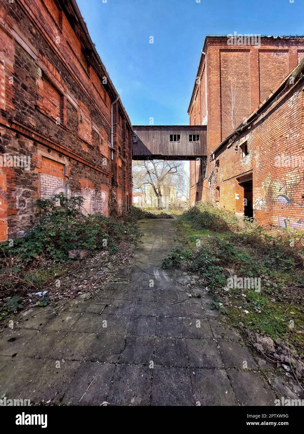 Durchgang zwischen zerstörten Fabrikgebäuden mit hölzerner Überführung. Stockfoto