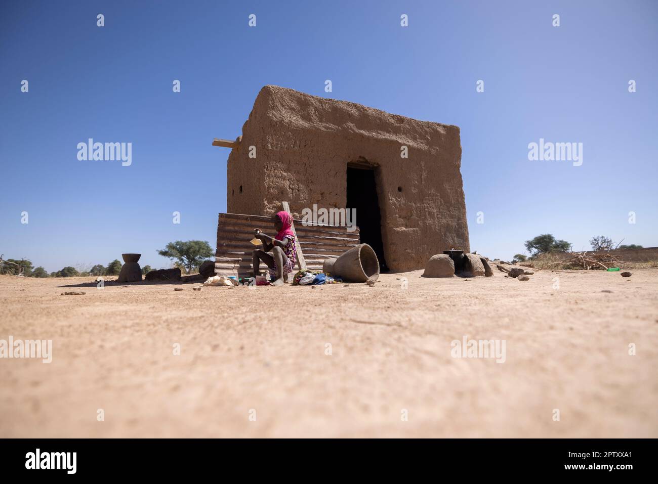 Irdenes Haus mit Kind, das draußen in der Region Segou, Mali, Westafrika, sitzt. 2022 Dürre und Hungerkrise in Mali. Stockfoto